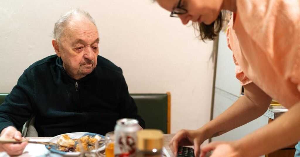 A caregiver assists an elderly man during mealtime at an indoor setting. Captured in Praha.