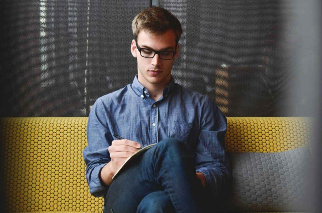 Digital marketing agency A young man in glasses writes in a notebook while sitting on a stylish couch indoors.