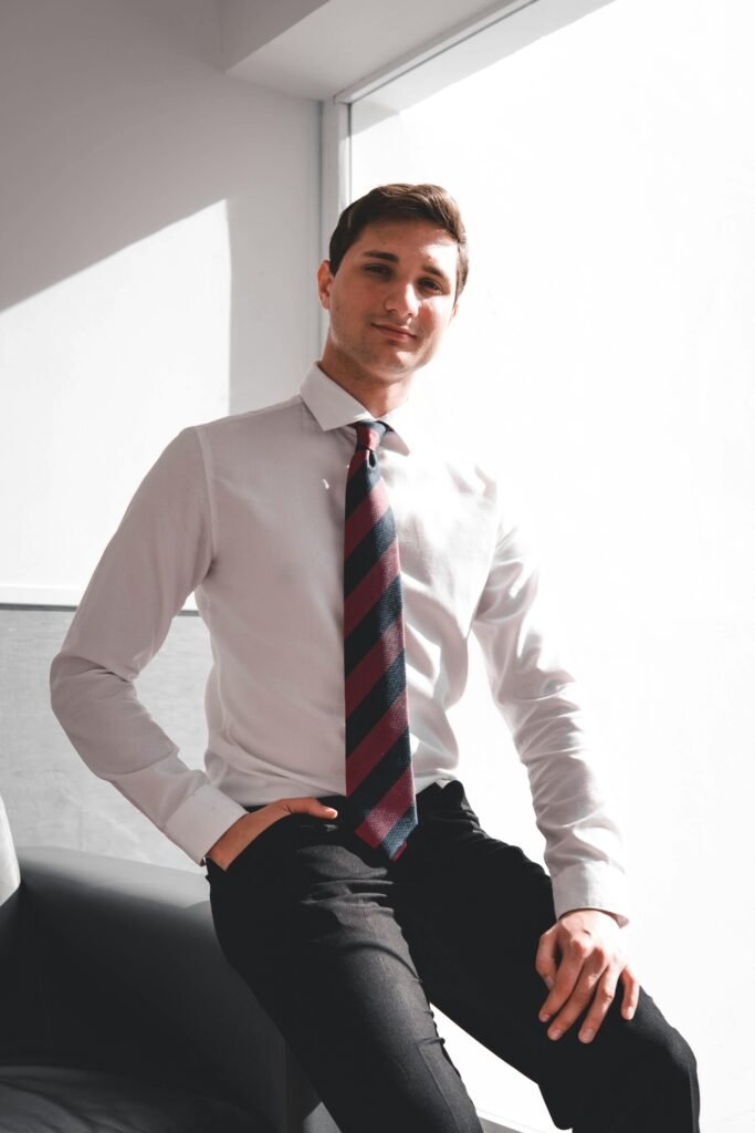 formal shirt for office wear Young man in formal business attire sitting confidently, illuminated by bright natural light.