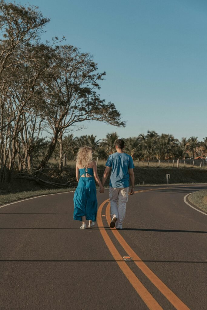 Couple walking hand in hand on a sunny road, surrounded by nature in Presidente Prudente, Brazil.