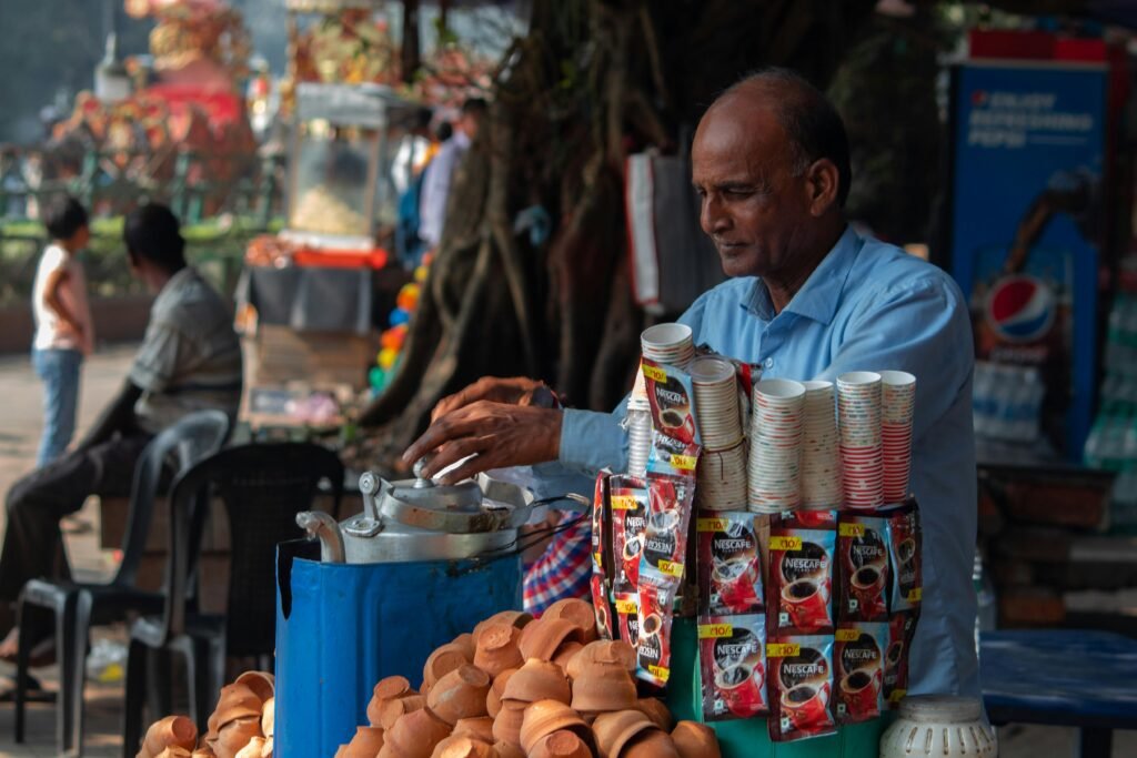 Street vendor in blue shirt serving chai in clay cups at a bustling outdoor market.