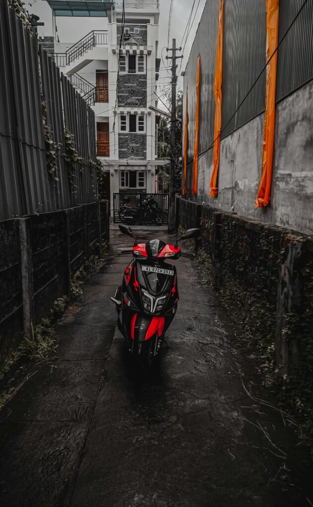 A moody urban alleyway in Kochi with a parked red scooter after rain, exuding an atmospheric vibe.
