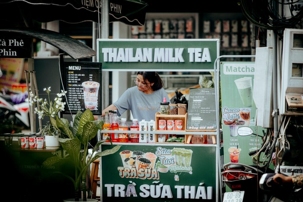 Street vendor at milk tea stall in bustling market offering Thai beverages.